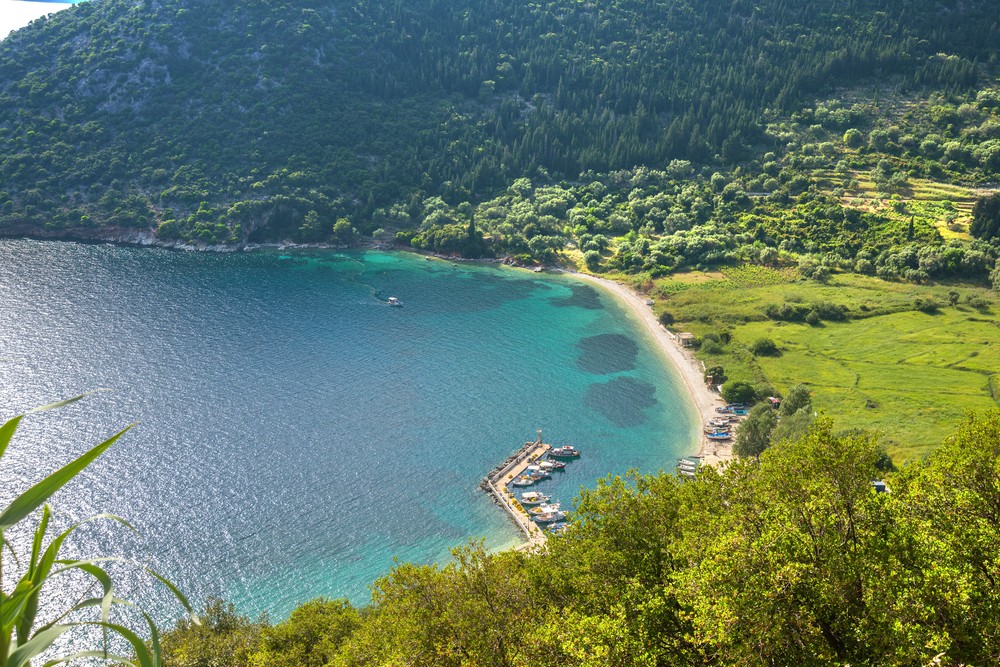 Polis: beach with green waters and dense vegetation. It is pebbly and a part of it is organized.